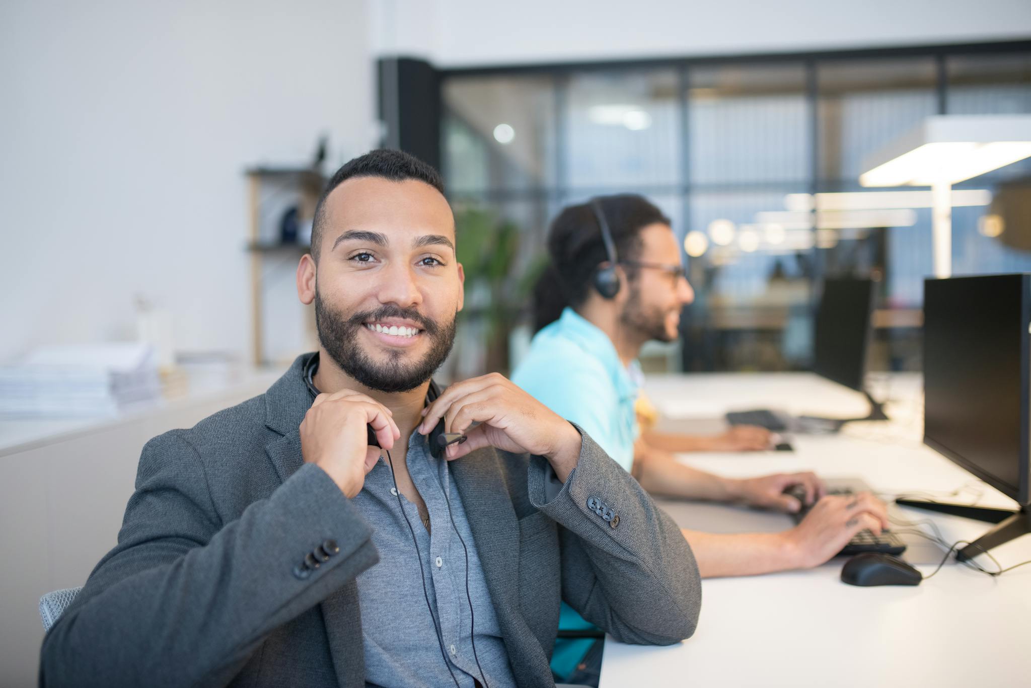 Two men in modern office setting with computers, headsets, and smiles, enhancing productivity.